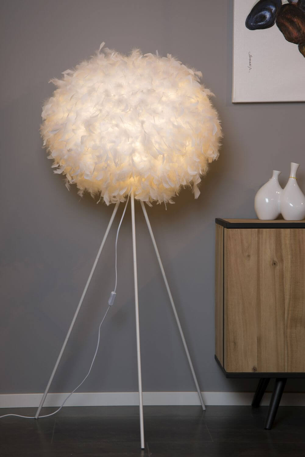 Vue de face du lampadaire boule en plumes allumé, posé près d'un meuble en bois.