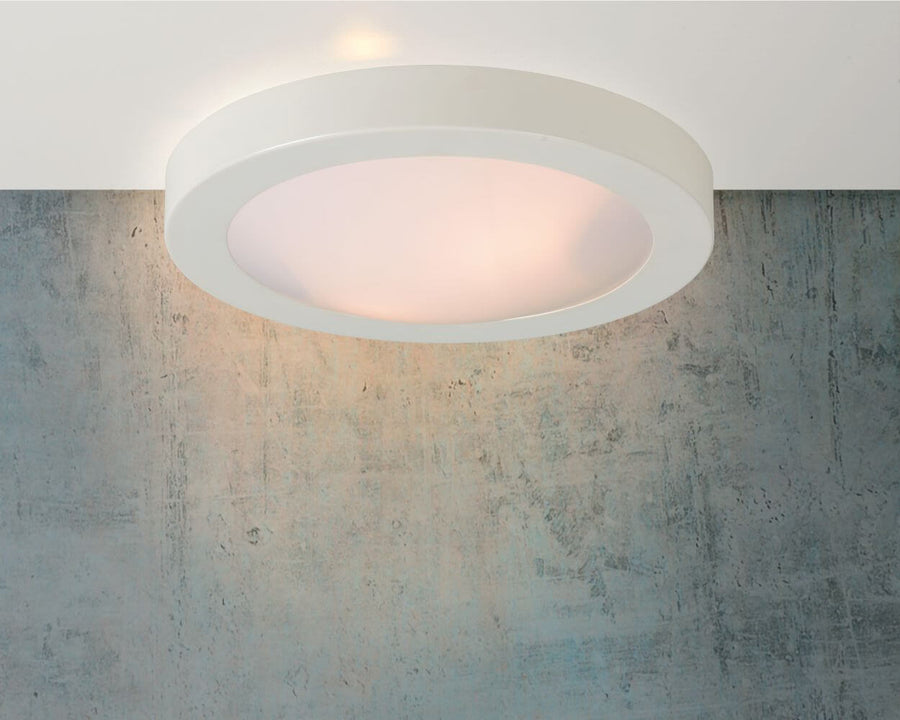 Plafonnier blanc installé au plafond devant un mur en béton, lumière allumée.