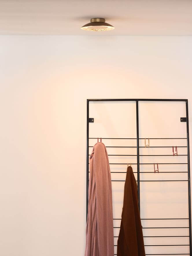 Plan rapproché du plafonnier doré monté au plafond, éclairant un mur blanc.