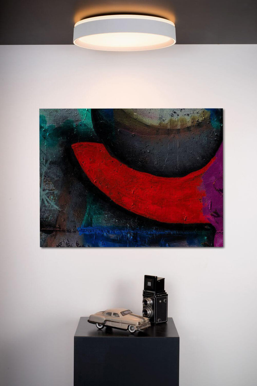 Vue rapprochée du plafonnier blanc allumé et de la toile abstraite colorée.