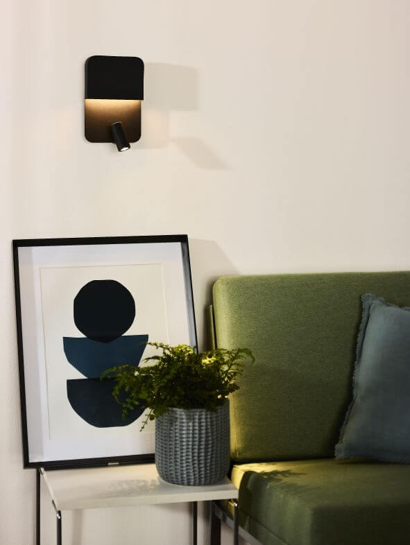 Applique murale noire allumée au-dessus d'une table et d'un fauteuil vert