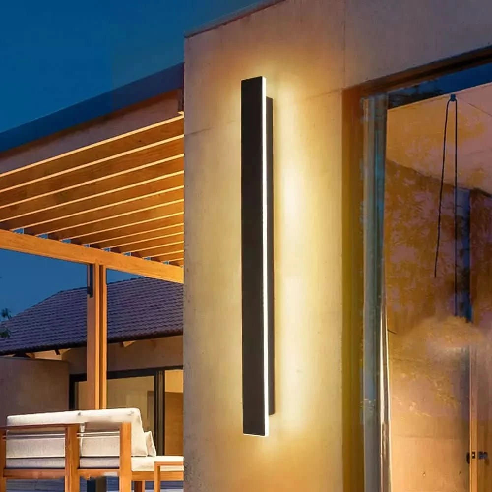 Ambiance de soirée sous pergola en bois, applique verticale allumée sur pilier beige