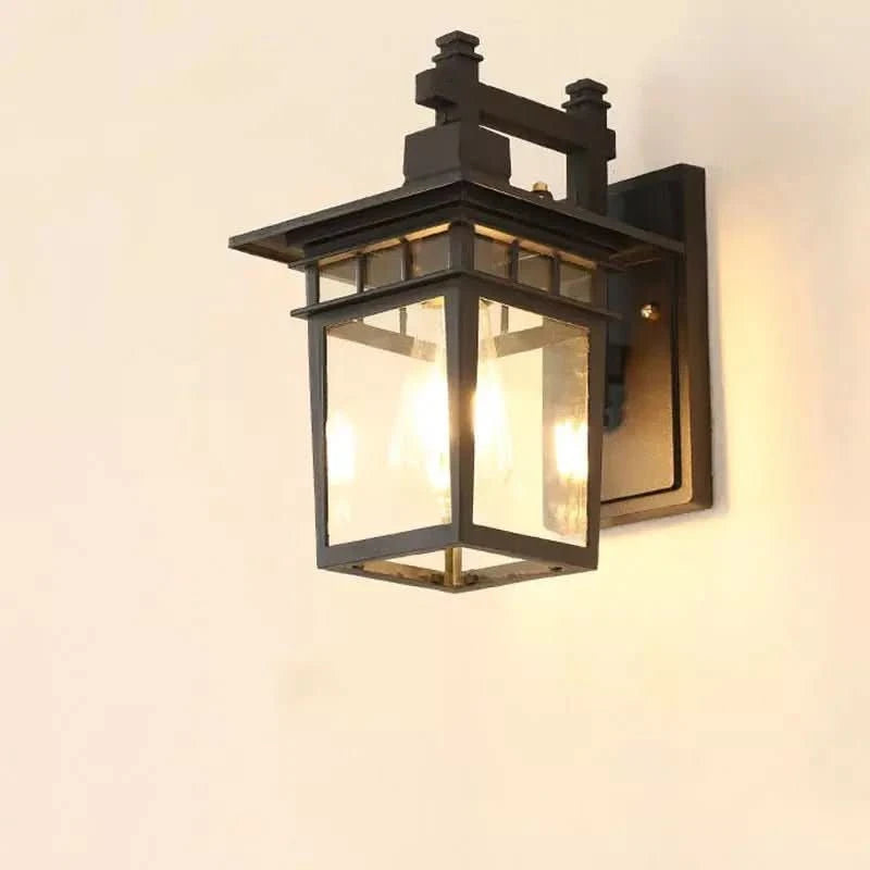 Luminaire mural noir à lanterne carrée, vitrage transparent et ampoule allumée sur fond clair