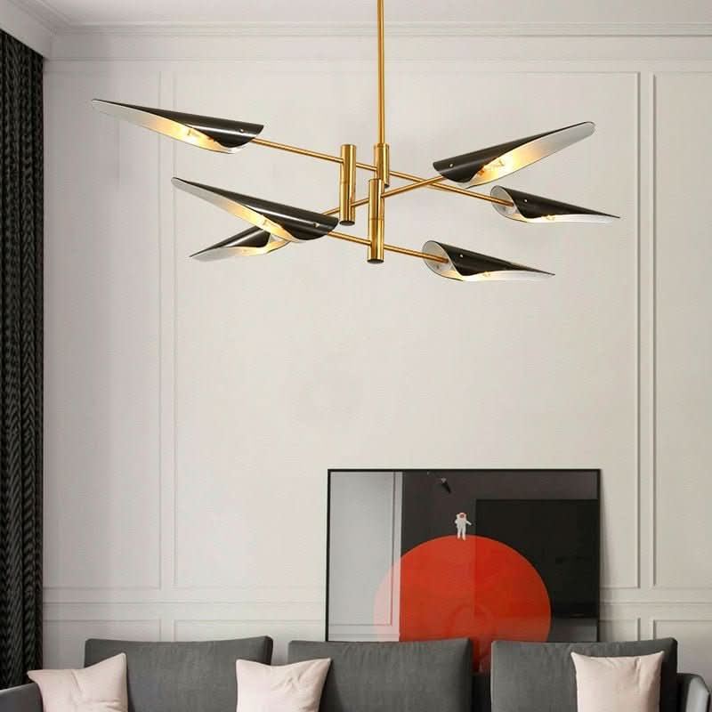 Lustre suspendu doré à six bras noirs éclairant un salon gris avec canapé et tableau.