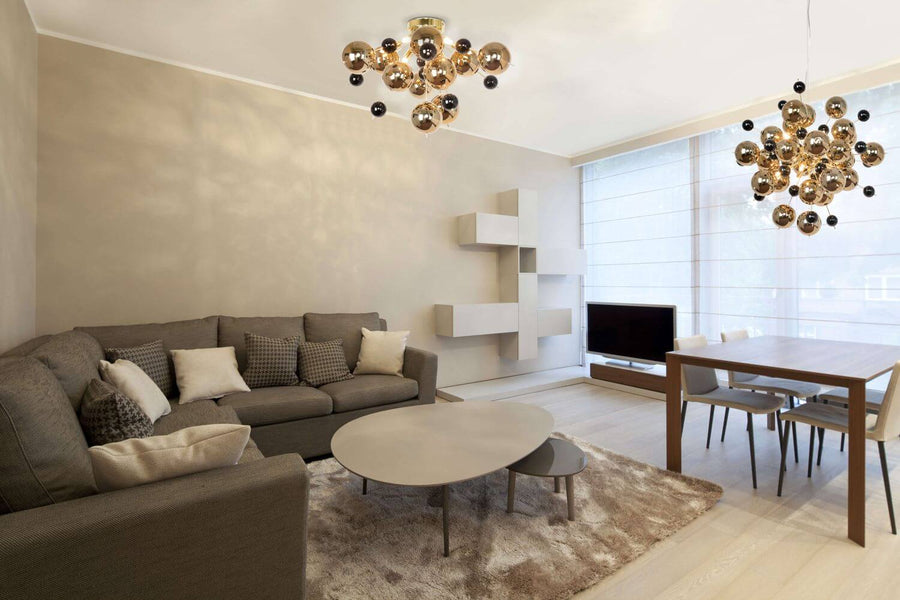 Plafonnier doré installé au plafond d'un salon, avec un luminaire suspendu en arrière-plan.