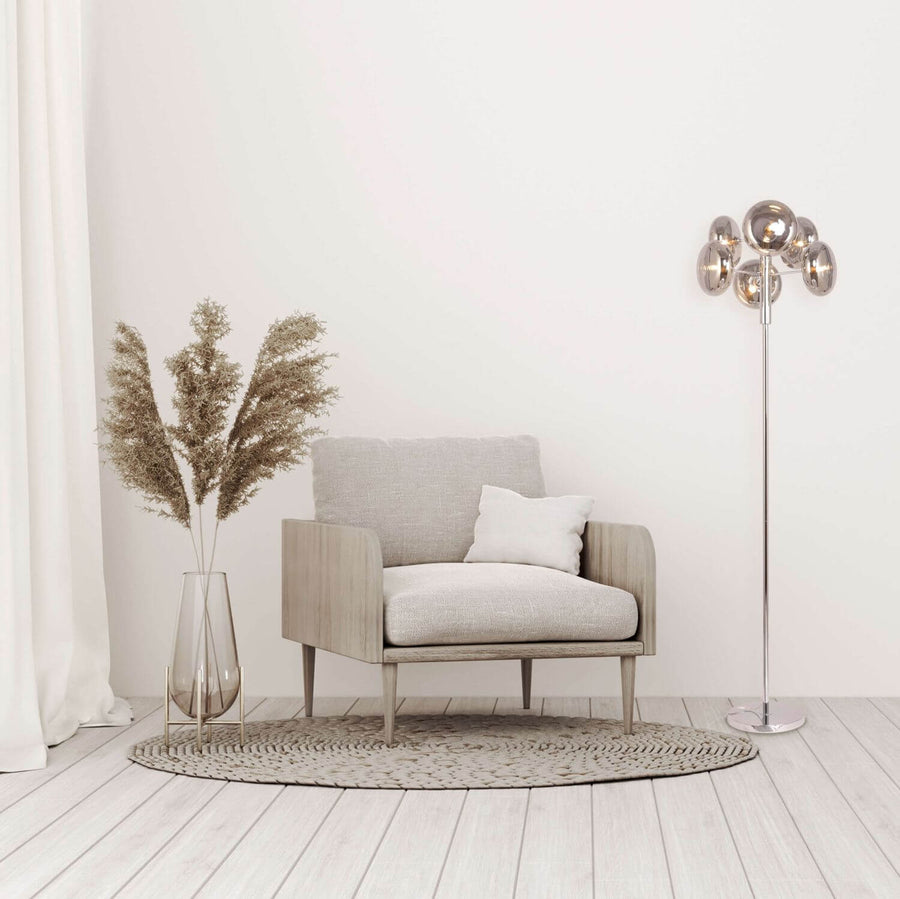 Lampadaire allumé près d'un fauteuil gris et d'un vase de graminées