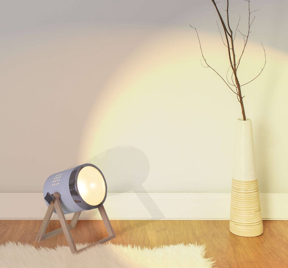 Mise en ambiance sur parquet, lampe éclairant le mur près d'un vase et de branches
