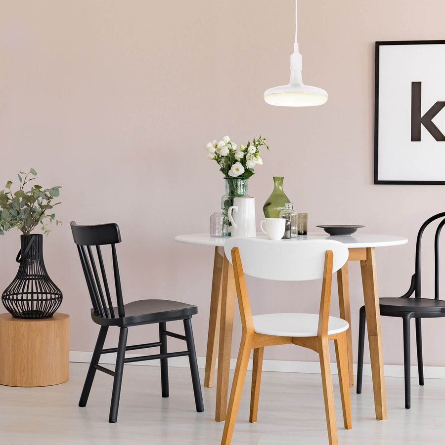 Luminaire suspendu blanc au-dessus d'une table ronde, chaises scandinaves et mur rose poudré