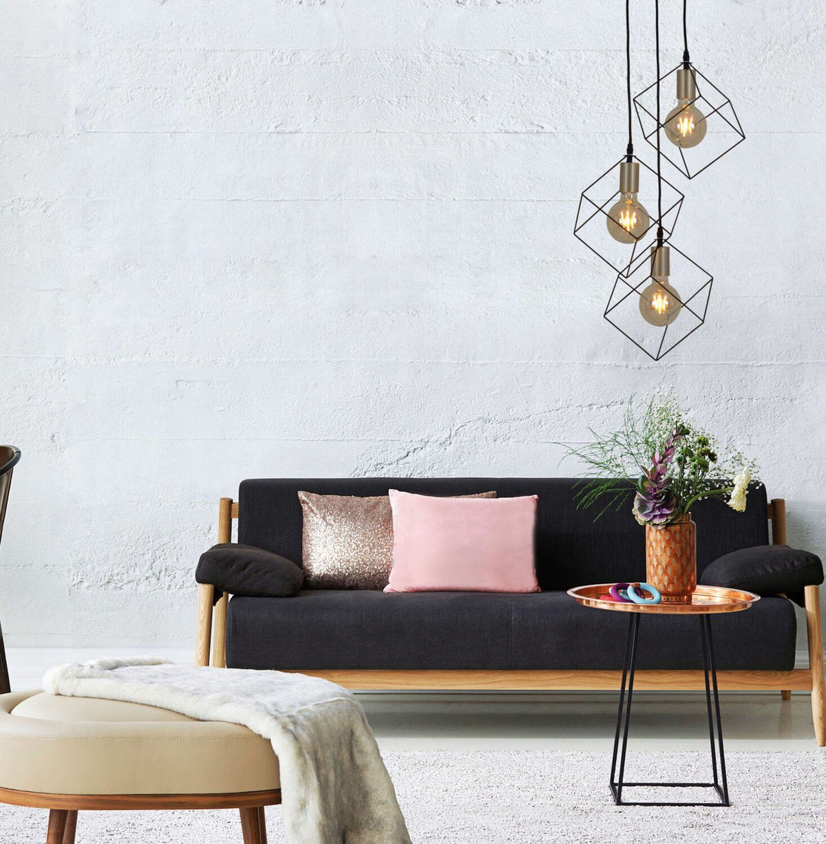 Mise en ambiance salon avec canapé noir, suspension à trois cages cubiques et ampoules Edison.