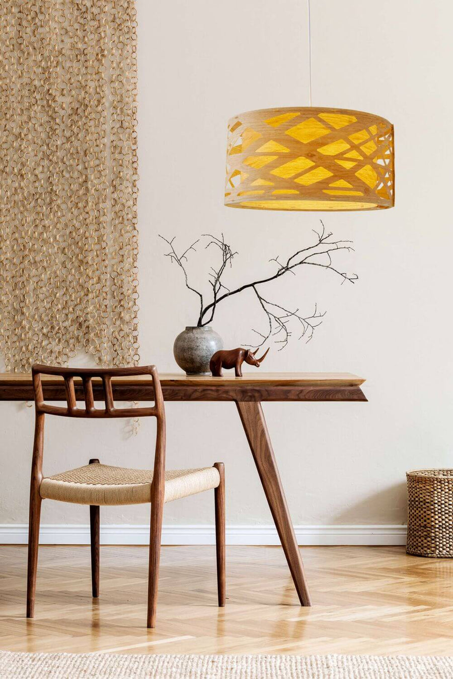 Suspension en bois allumée dans un intérieur avec table, chaise, vase et branche sèche.