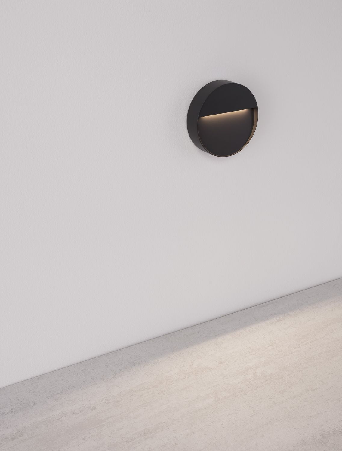 Applique murale ronde noire allumée, fixée sur un mur blanc avec sol béton clair