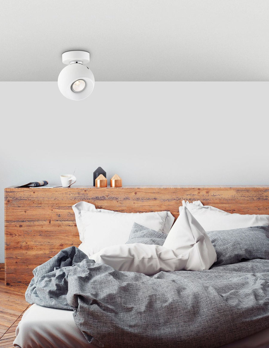 Plafonnier blanc sphérique installé au plafond dans une chambre, au-dessus d'un lit en bois clair.