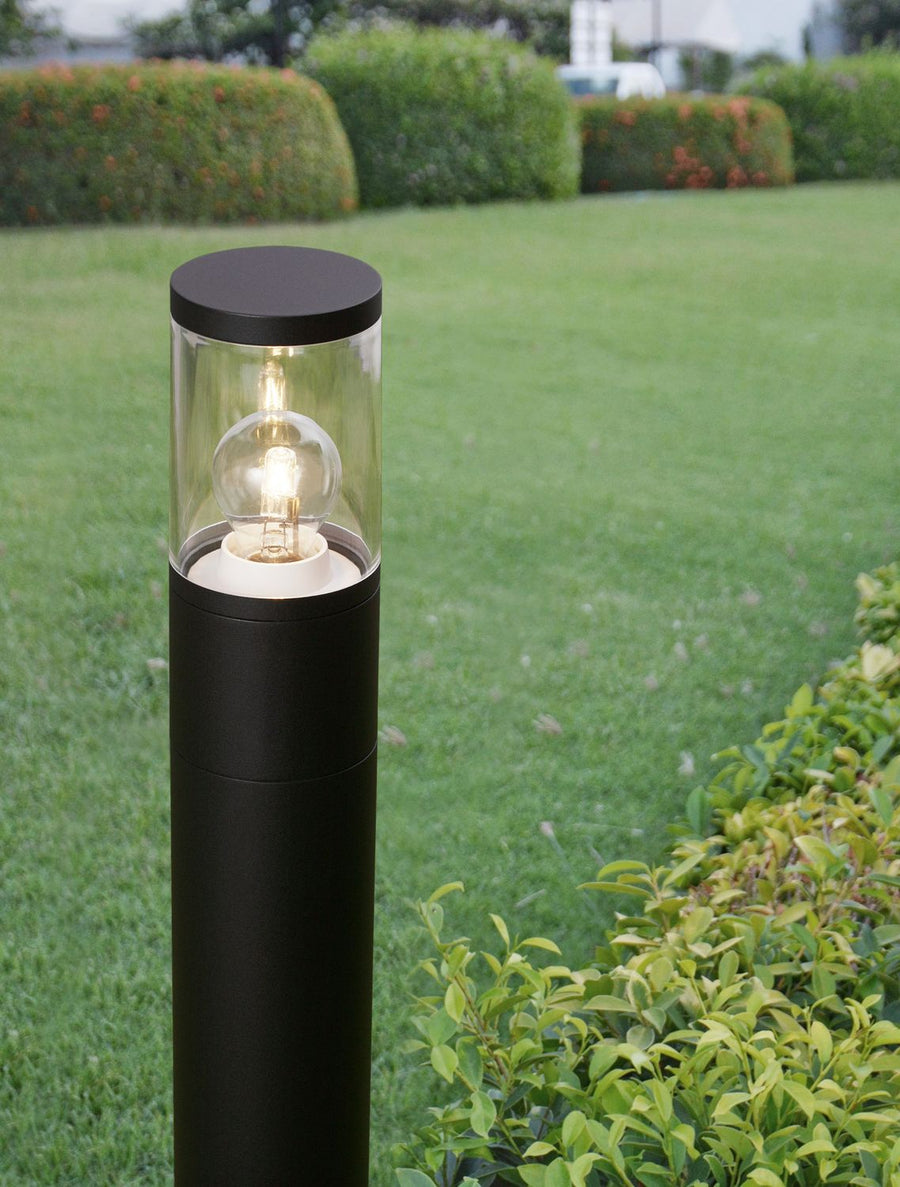 Gros plan de la borne noire allumée dans un jardin, tête transparente et ampoule visibles