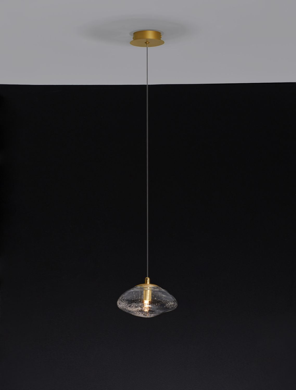 Suspension dorée fixée au plafond, verre bullé allumé sur fond noir