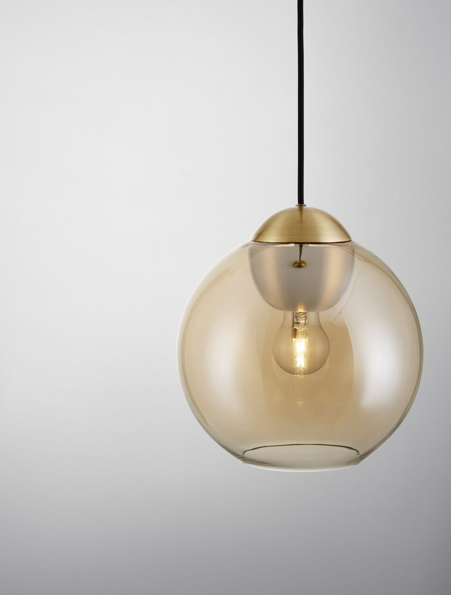 Suspension dorée avec globe en verre ambré et ampoule visible, vue de face sur fond clair