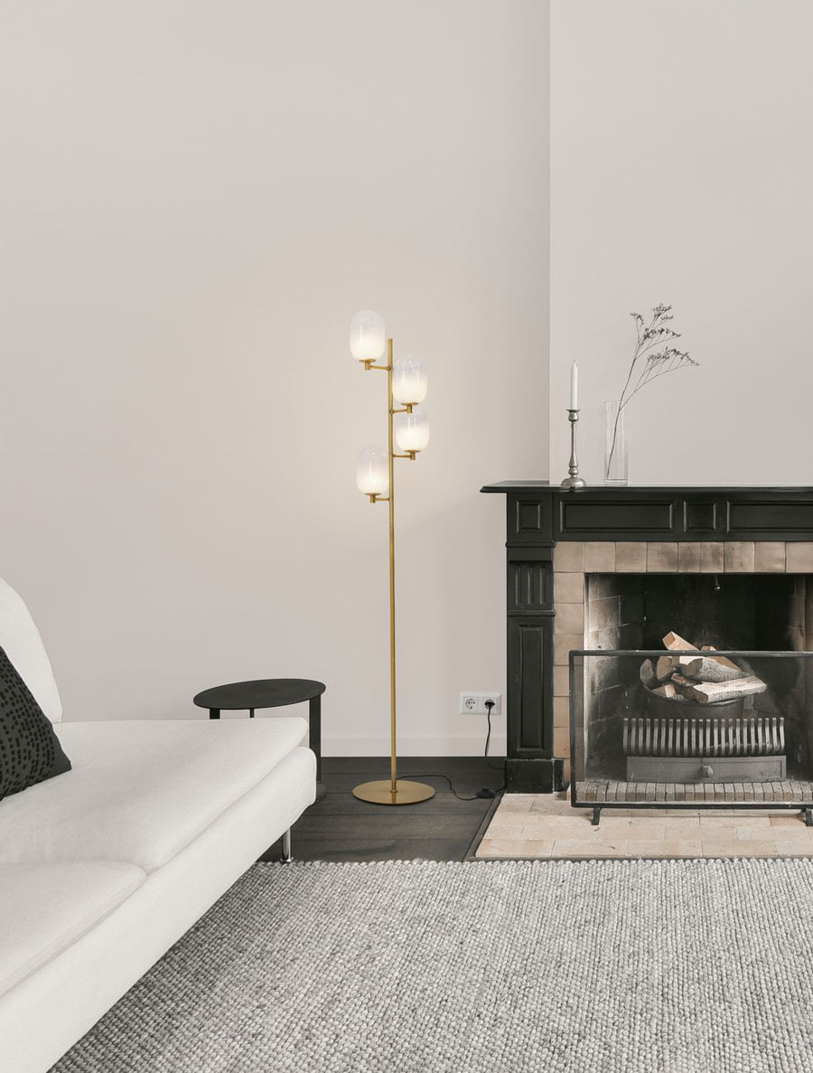 Lampadaire doré à quatre globes posé dans un salon devant une cheminée noire