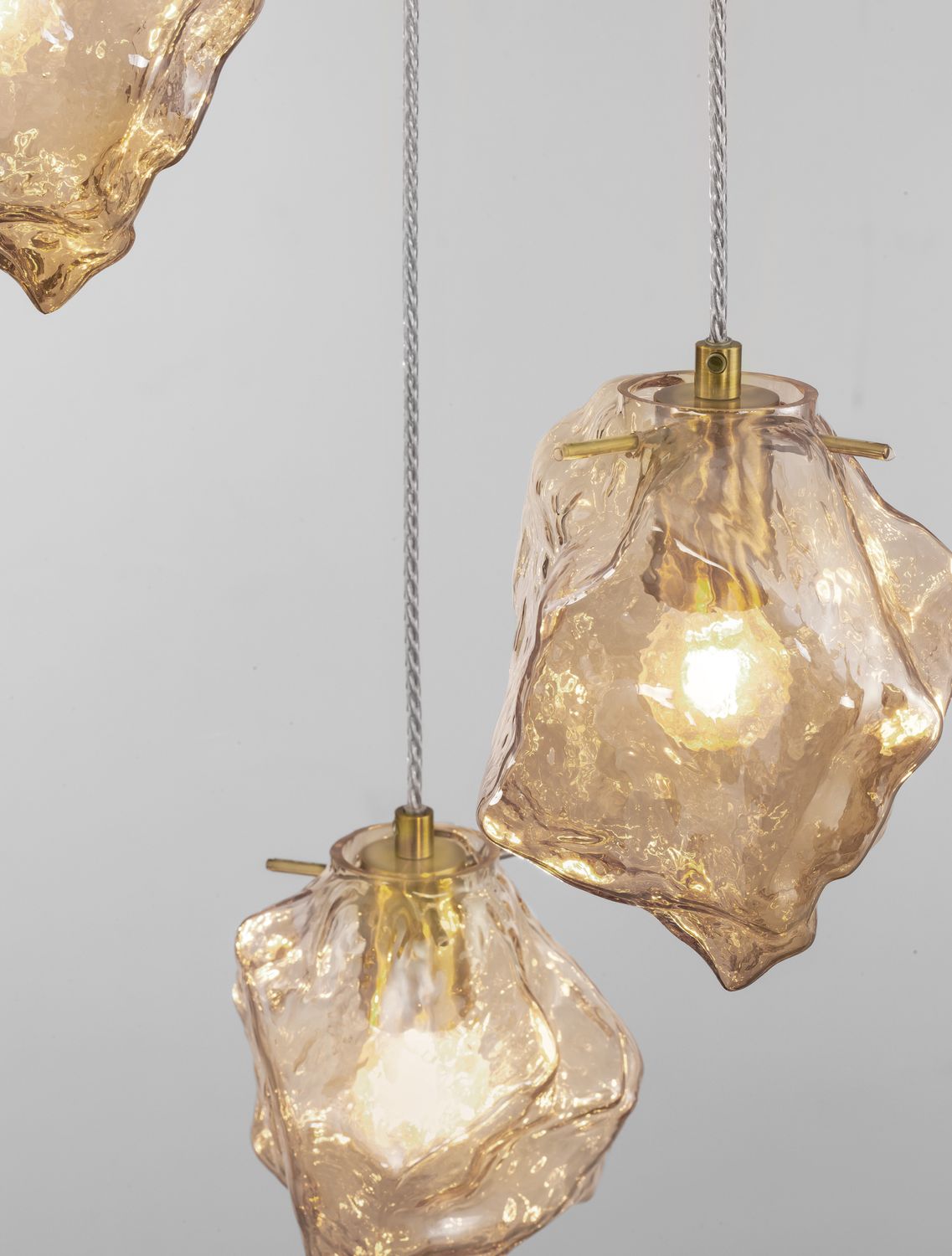 Gros plan sur deux diffuseurs en verre ambré martelé, ampoules allumées, suspension dorée