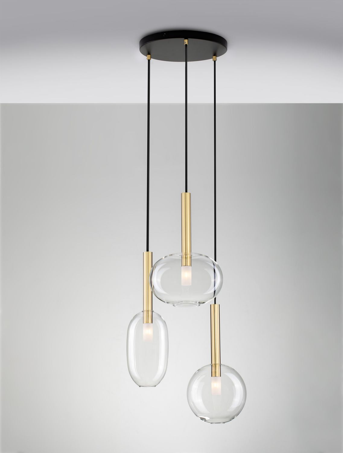 Trois suspensions allumées sur fond gris, diffusant une lumière chaude dans le verre