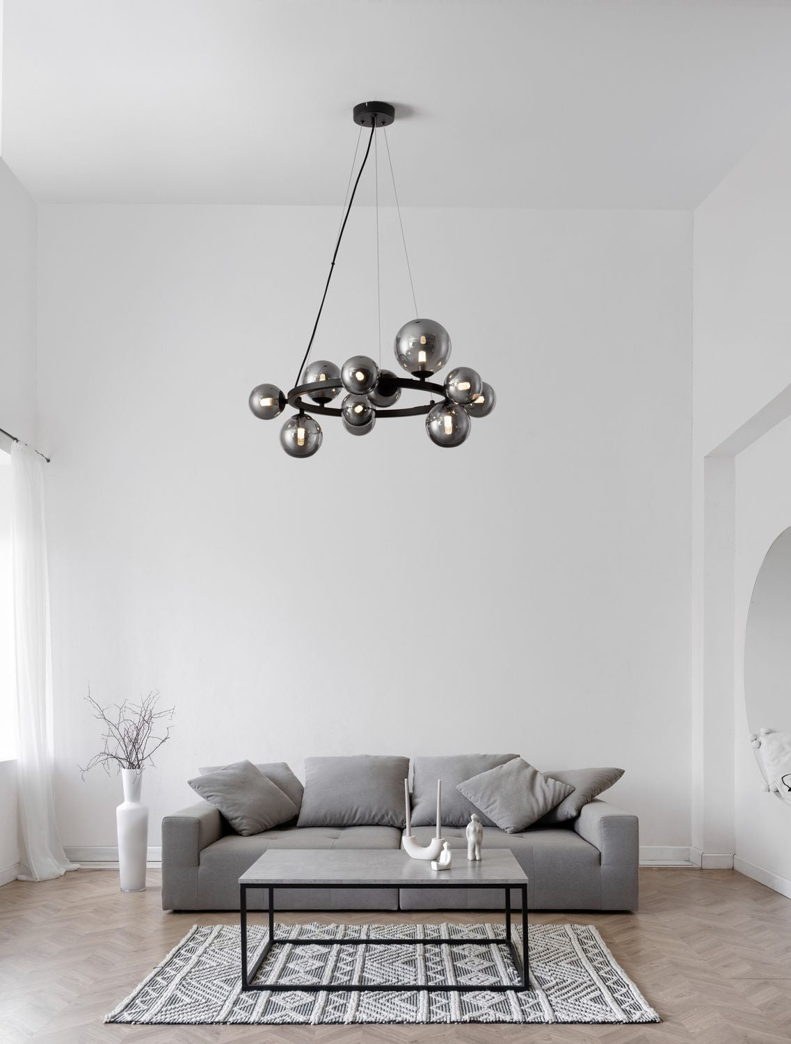 Suspension allumée au-dessus d'un canapé gris dans un salon épuré et lumineux