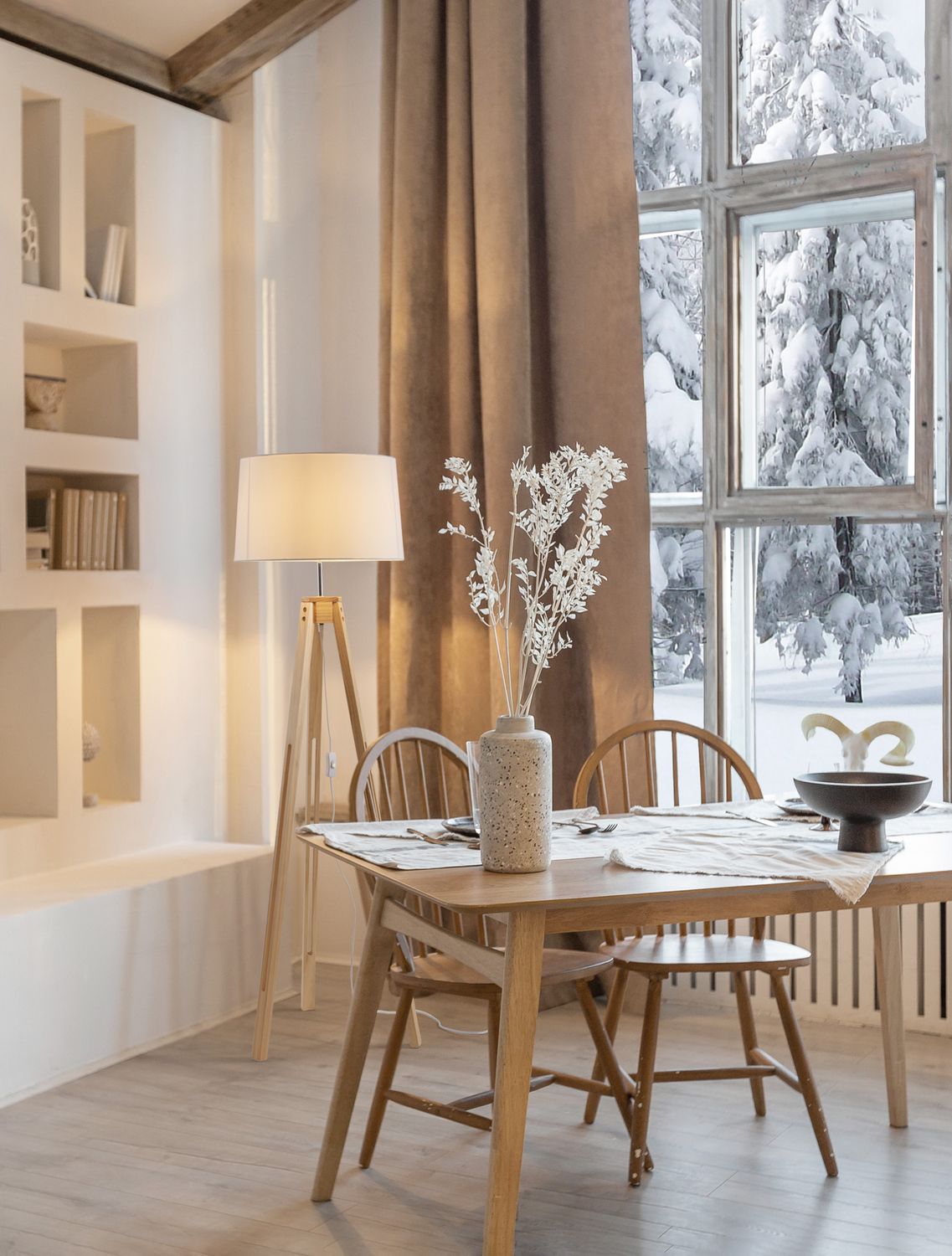 Lampadaire en bois dans une salle à manger lumineuse face à une fenêtre enneigée