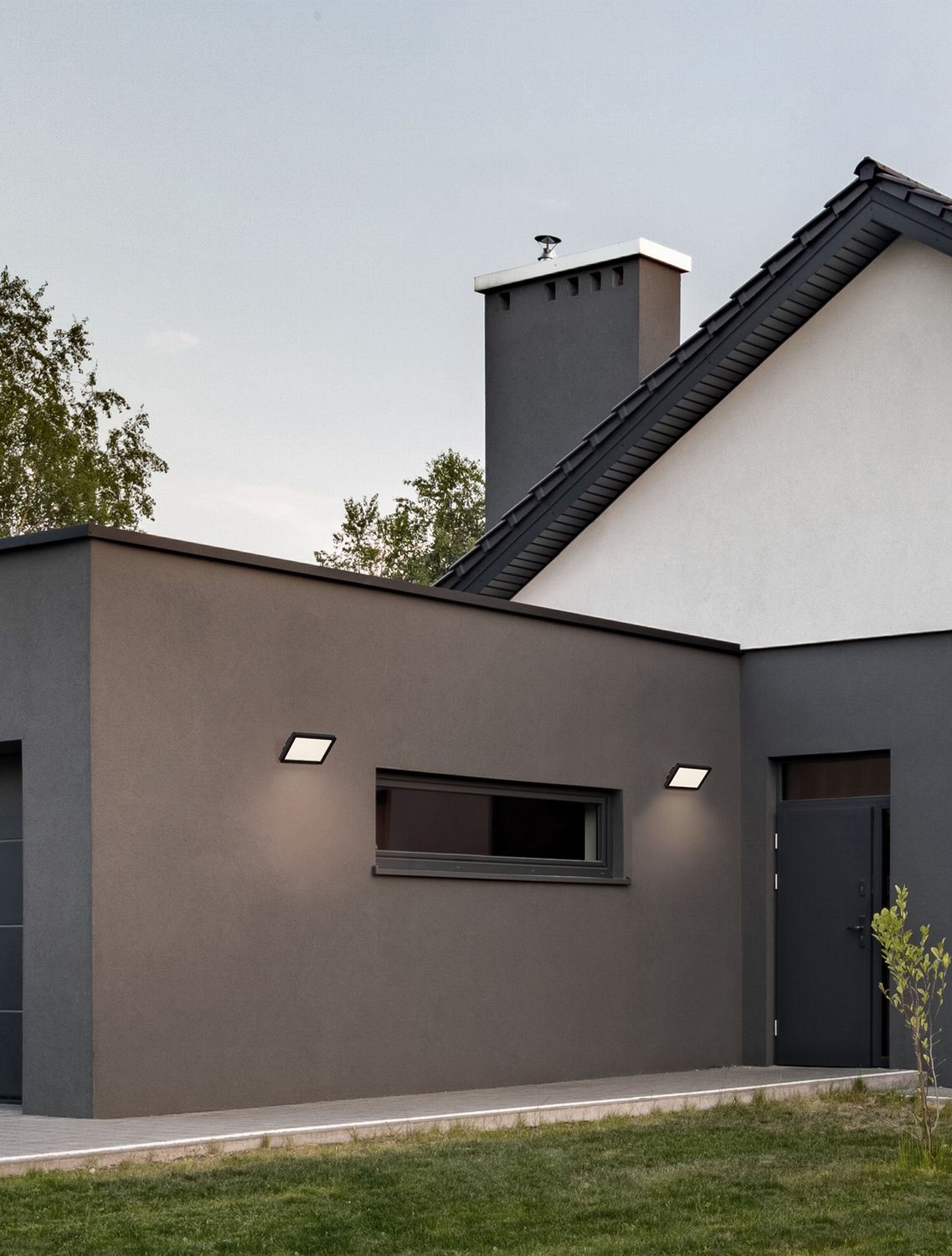 Applique murale noire allumée sur la façade grise d'une maison moderne