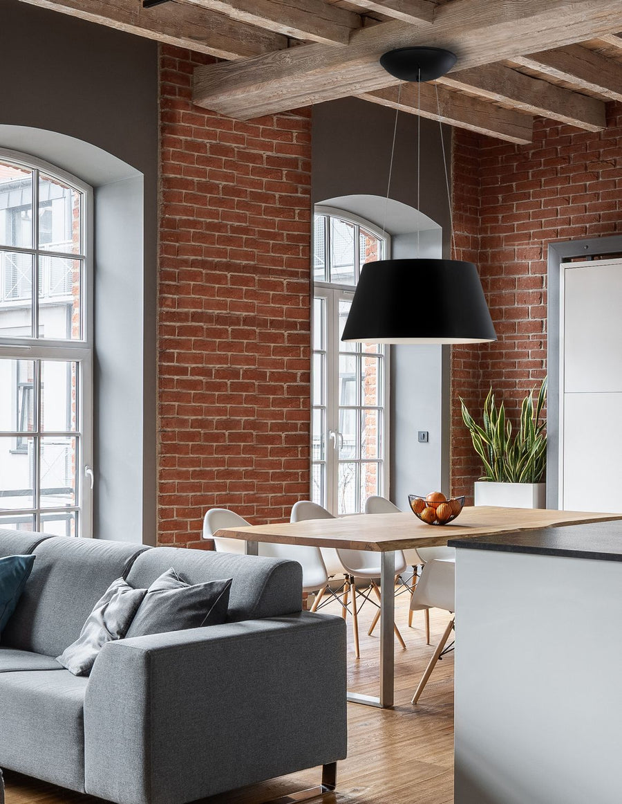 Suspension noire allumée au-dessus d'une table dans un loft en briques rouges
