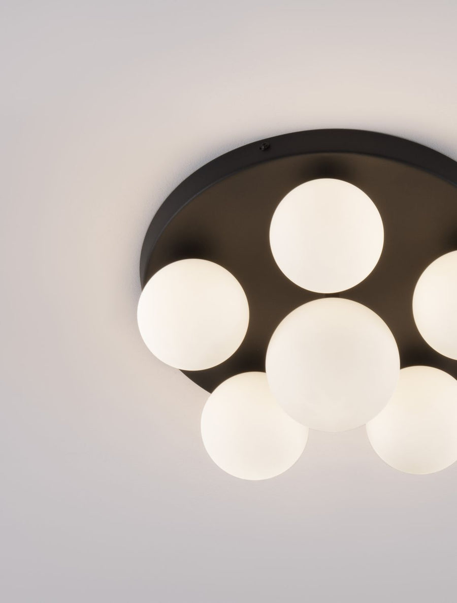 Détail rapproché de la finition noire mate et des globes en verre blanc