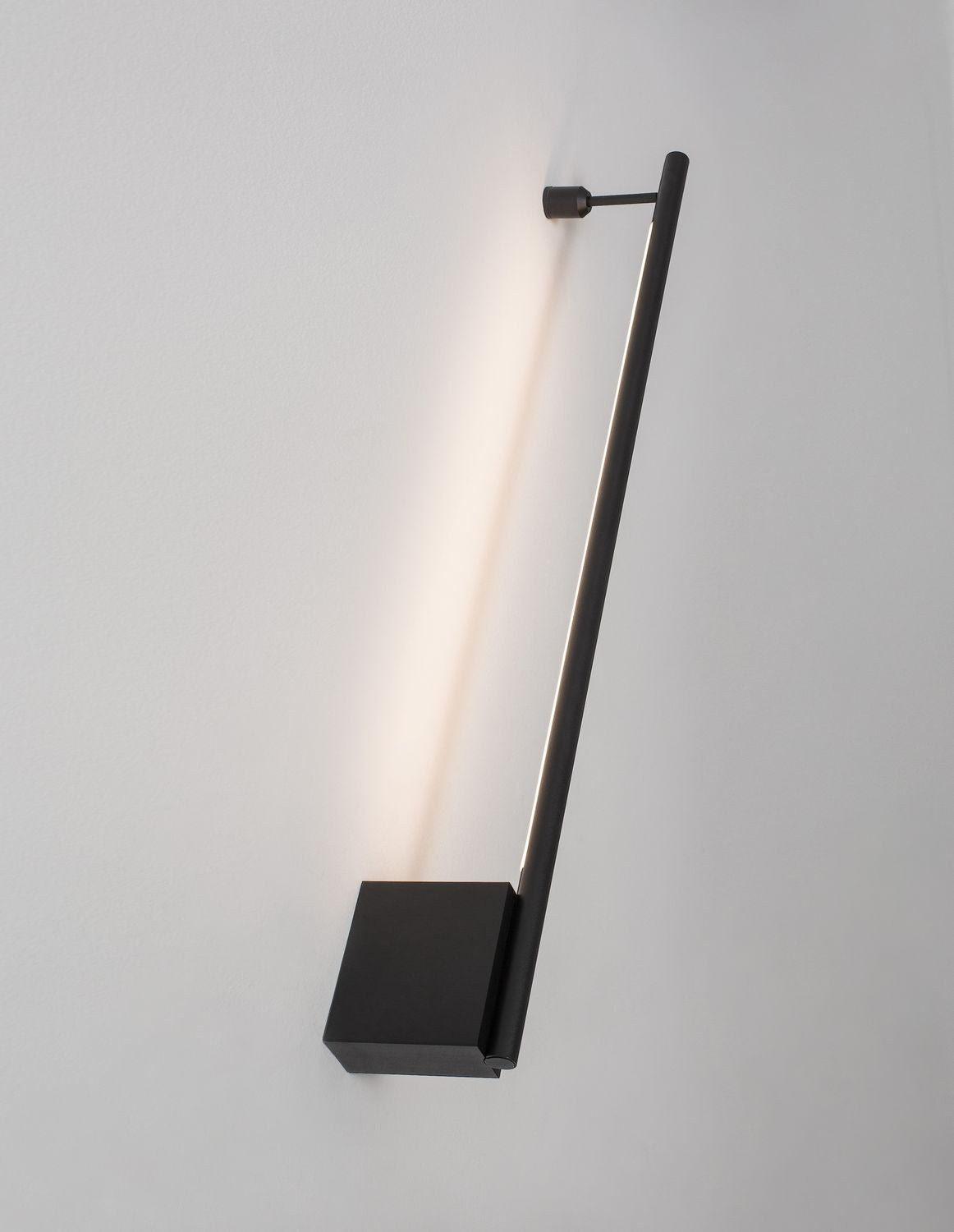Applique murale noire inclinée sur mur blanc, halo de lumière vertical diffusé en haut