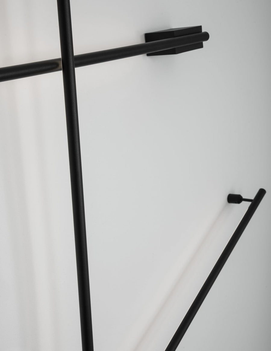 Vue en situation d'une applique murale noire aux tubes entrecroisés sur un mur blanc