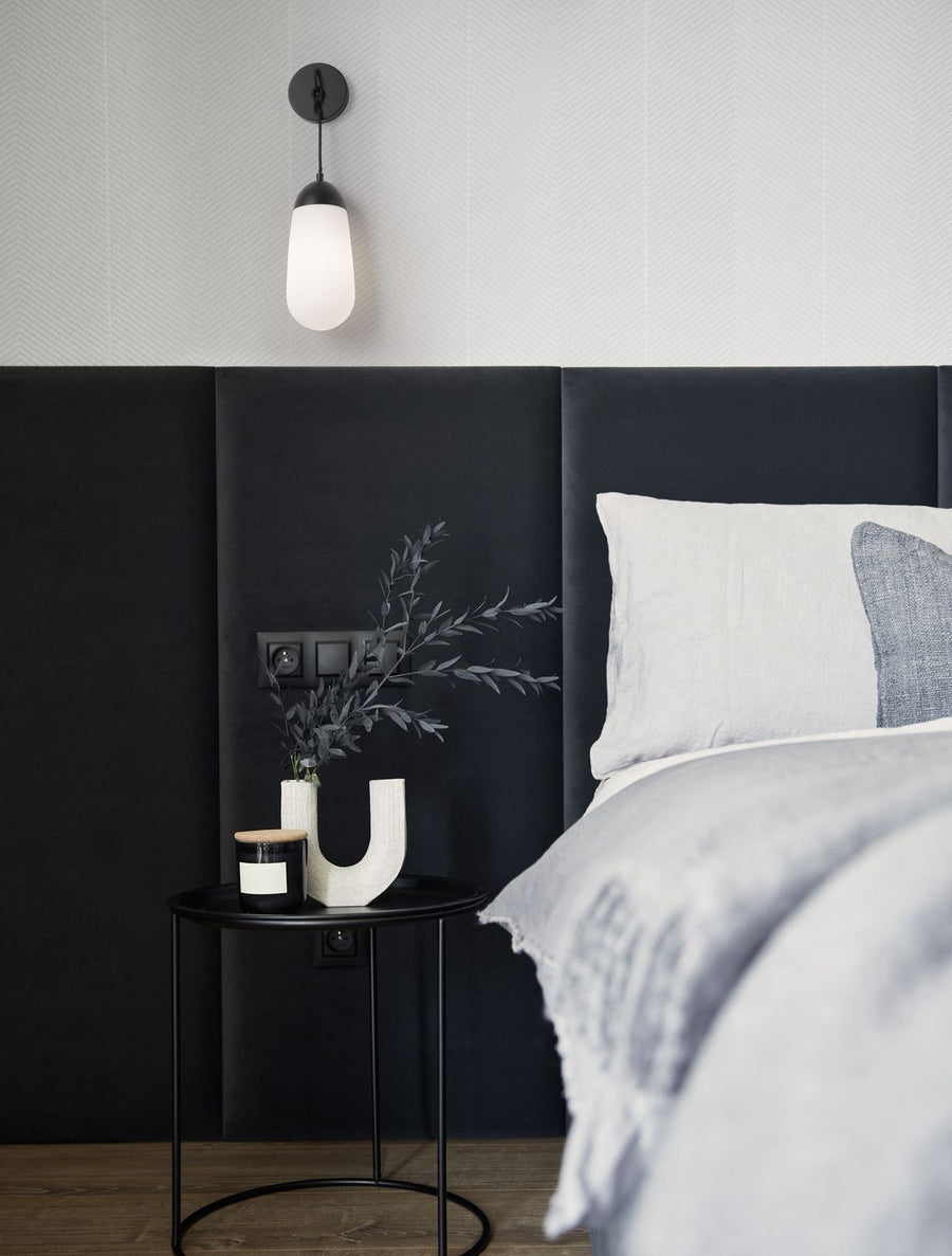 Applique murale noire allumée au-dessus d'une table de chevet dans une chambre sombre