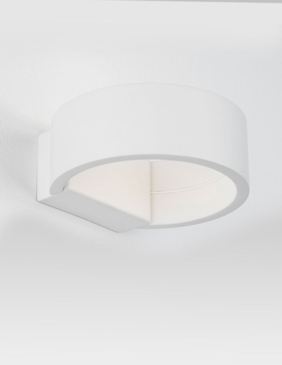 Luminaire mural blanc en métal vu de trois quarts, éclairage diffus vers le bas.