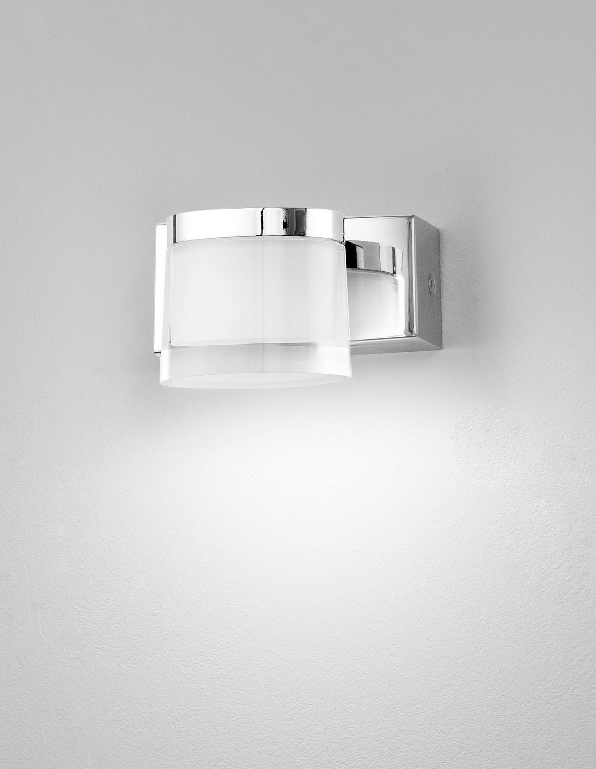 Applique murale chromée allumée sur mur blanc, halo lumineux diffus vers le bas