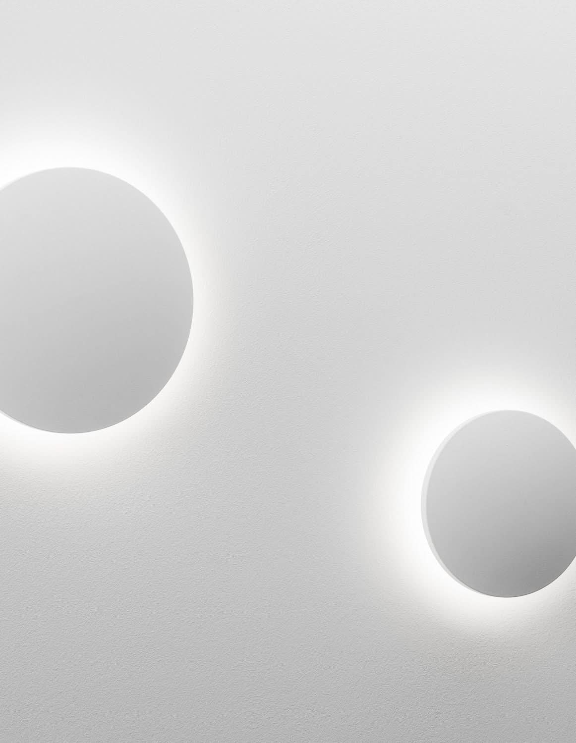 Deux appliques rondes blanches allumées, halos lumineux sur mur gris clair