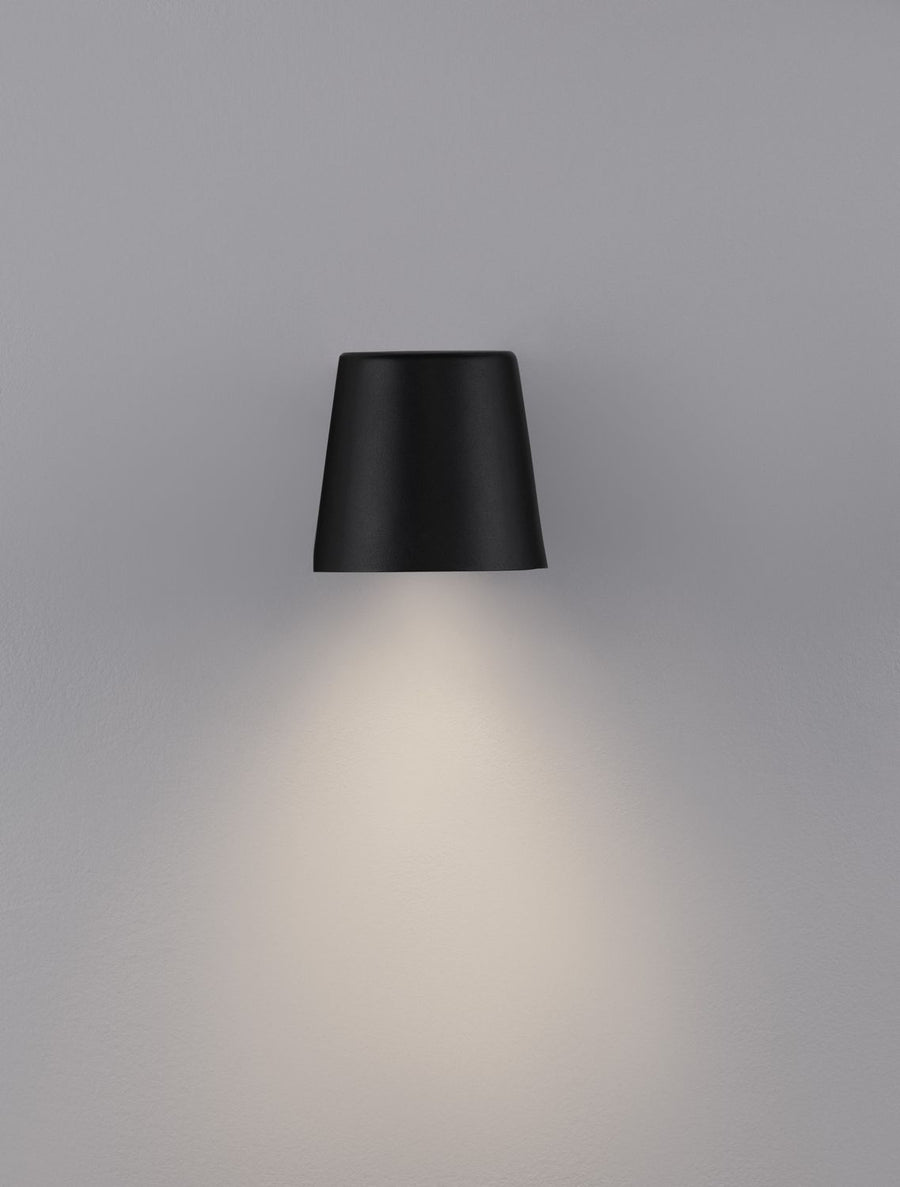 Applique allumée projetant un halo de lumière chaude vers le bas sur le mur