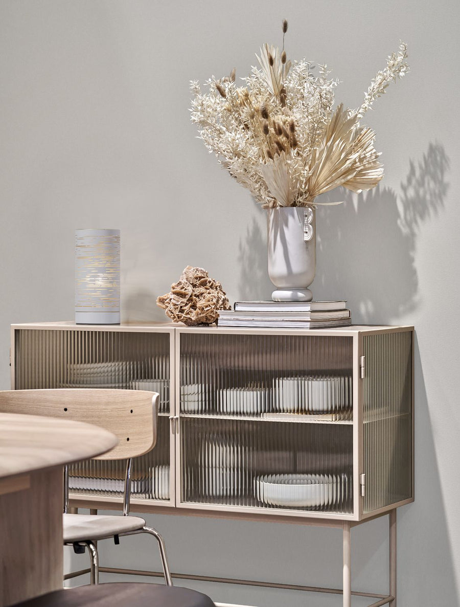 Lampe cylindrique blanche posée sur un buffet en bois, décor de fleurs séchées