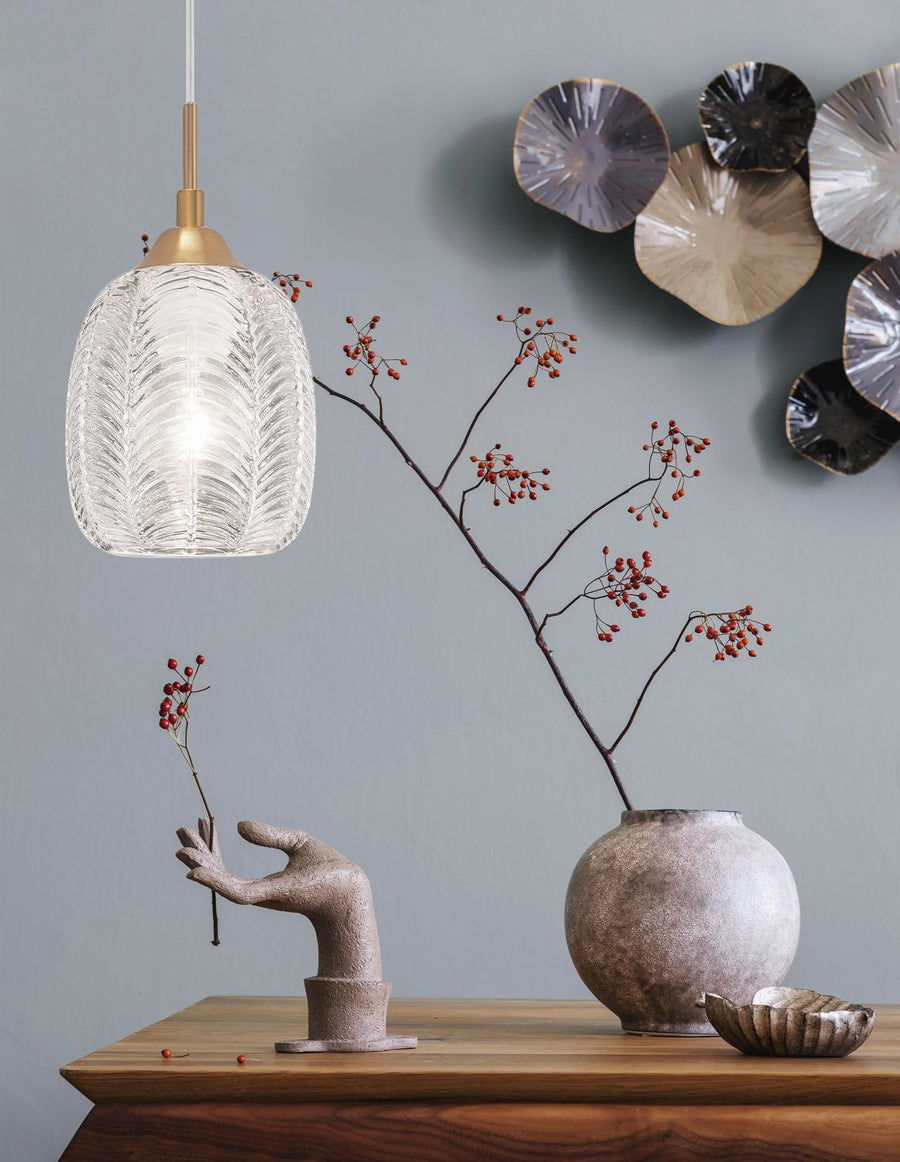 Suspension dorée allumée dans un décor avec vase, branche à baies rouges et main sculptée