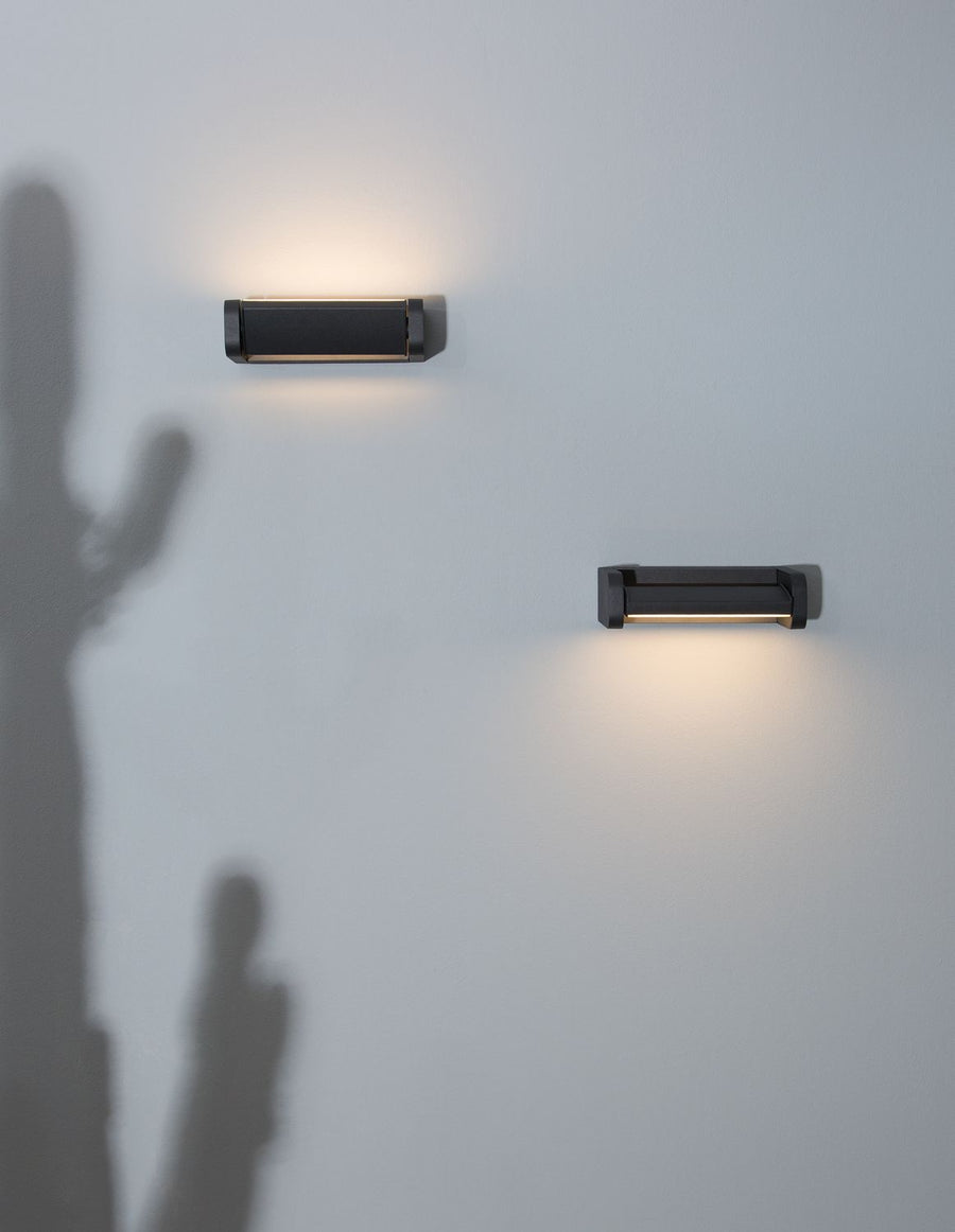 Vue de trois-quarts de l'applique noire fixée sur un mur gris clair