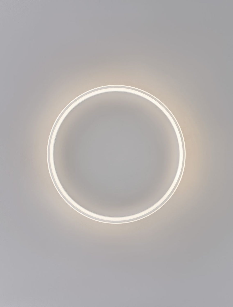 Plafonnier rond allumé, anneau lumineux blanc sur fond gris neutre.