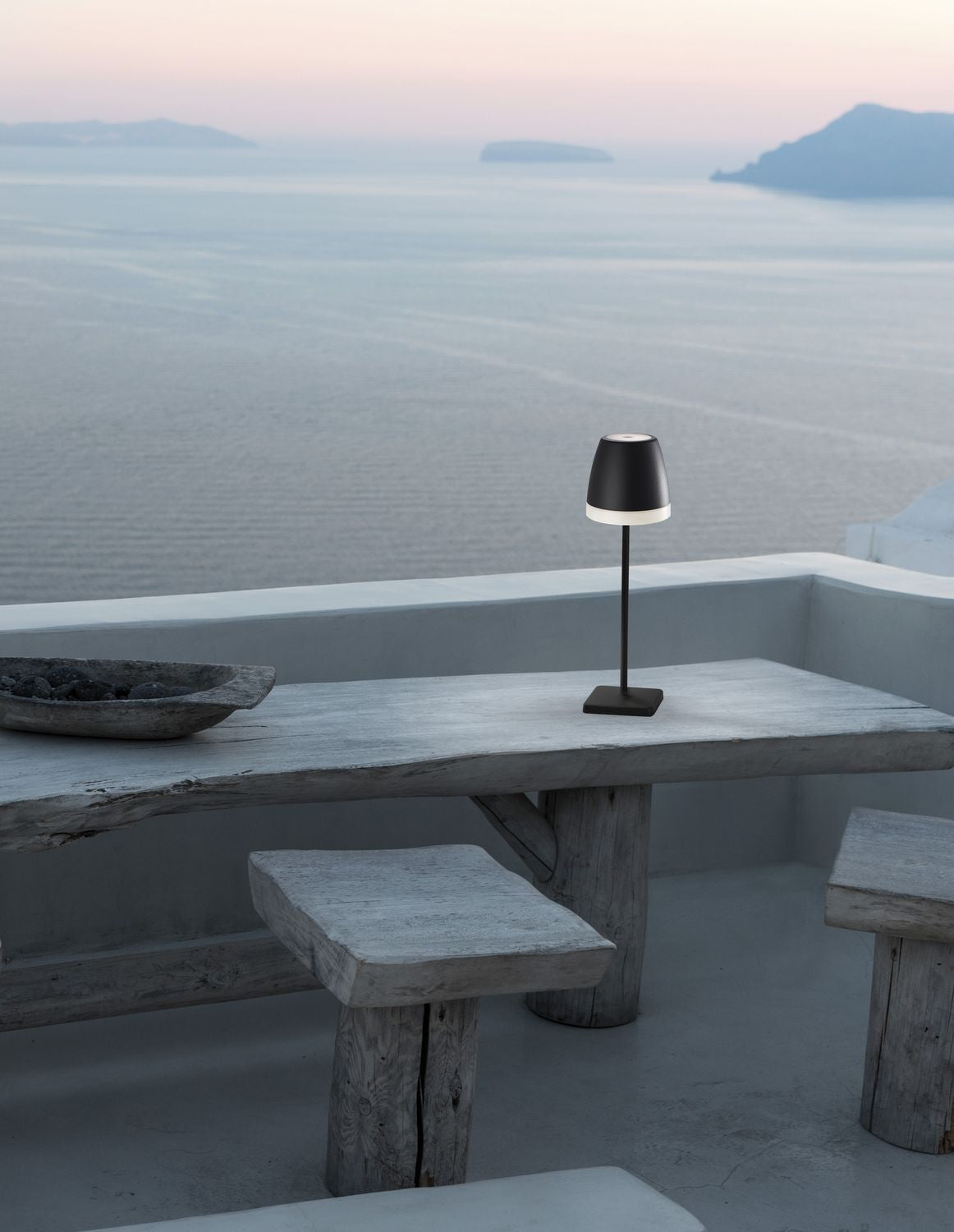 Lampe noire posée sur table en bois, vue sur la mer et les îles