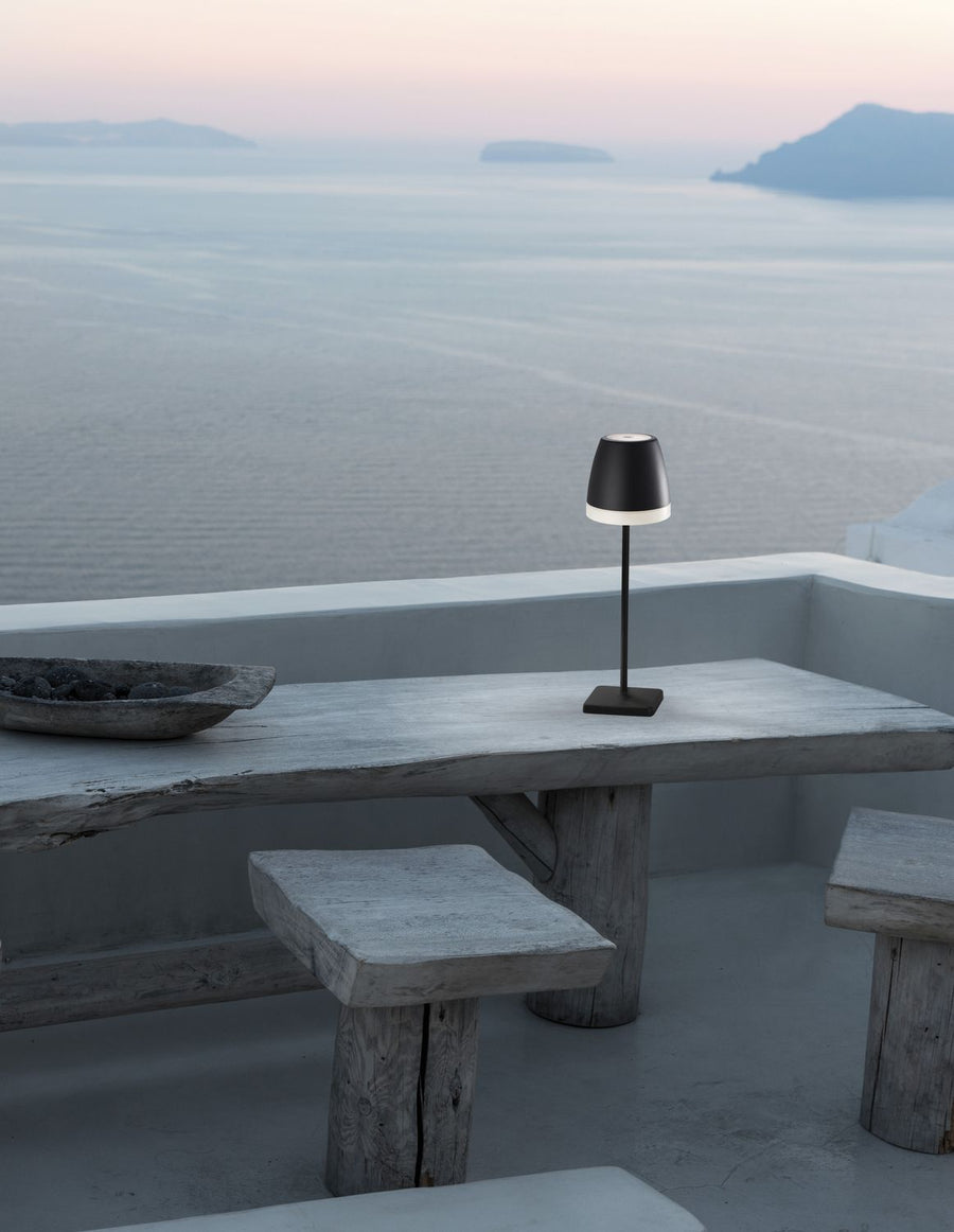Lampe noire posée sur table en bois, vue sur la mer et les îles
