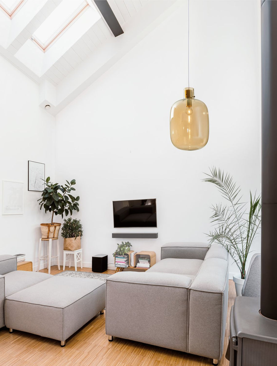 Suspension dorée allumée dans un salon blanc avec canapé et plantes