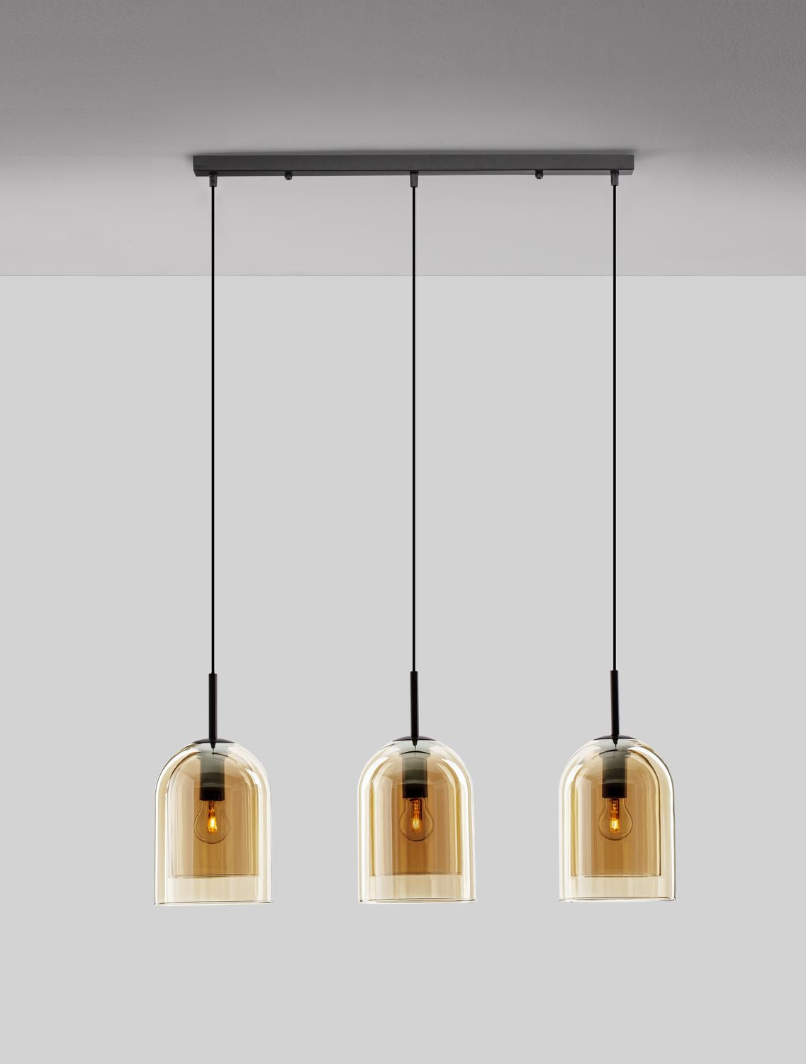 Suspension trois lumières vue de face sur fond gris, verre ambré et structure noire