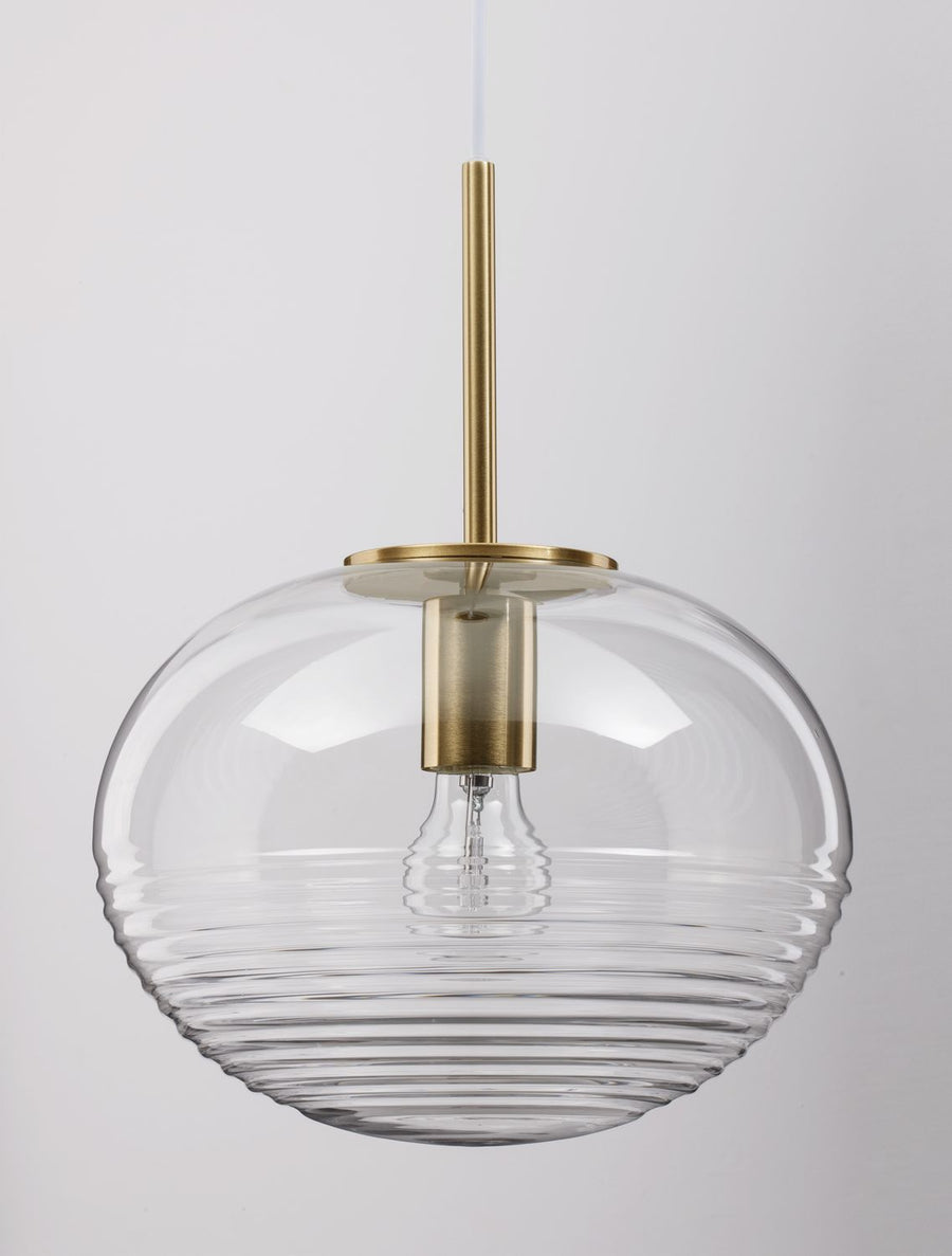 Gros plan sur l'abat-jour sphérique en verre strié et la douille dorée avec ampoule allumée