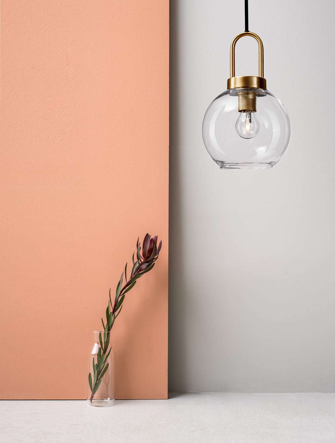 Suspension dorée en verre transparent devant un mur corail, mise en ambiance chaleureuse