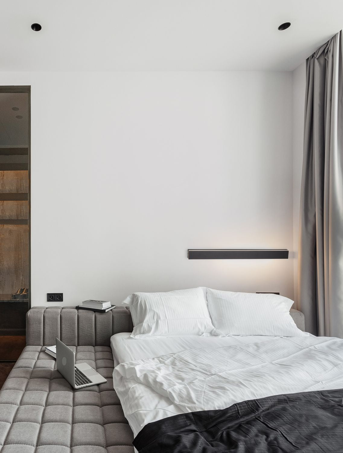 Applique murale noire allumée au-dessus d'un lit, ambiance chambre moderne et épurée