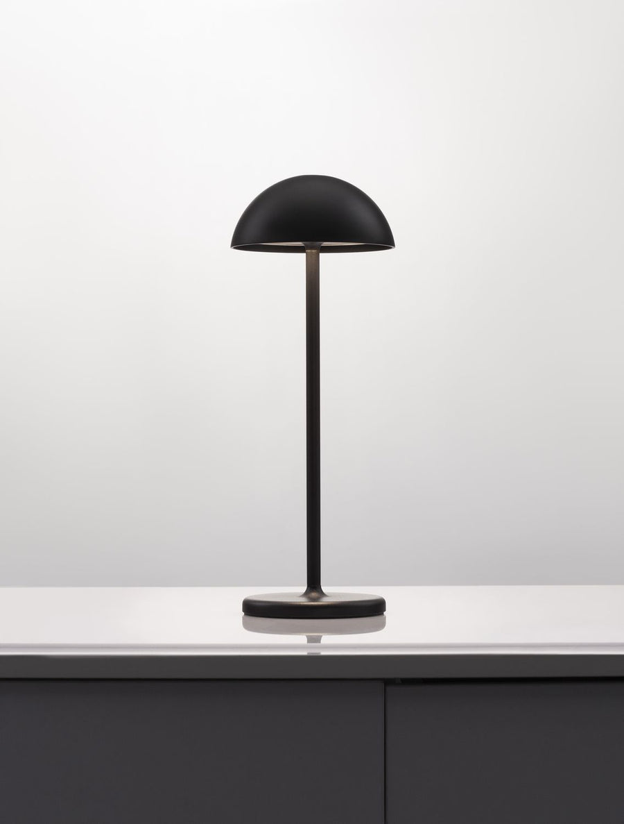Même lampe noire en situation sur un meuble, lumière peut-être allumée.