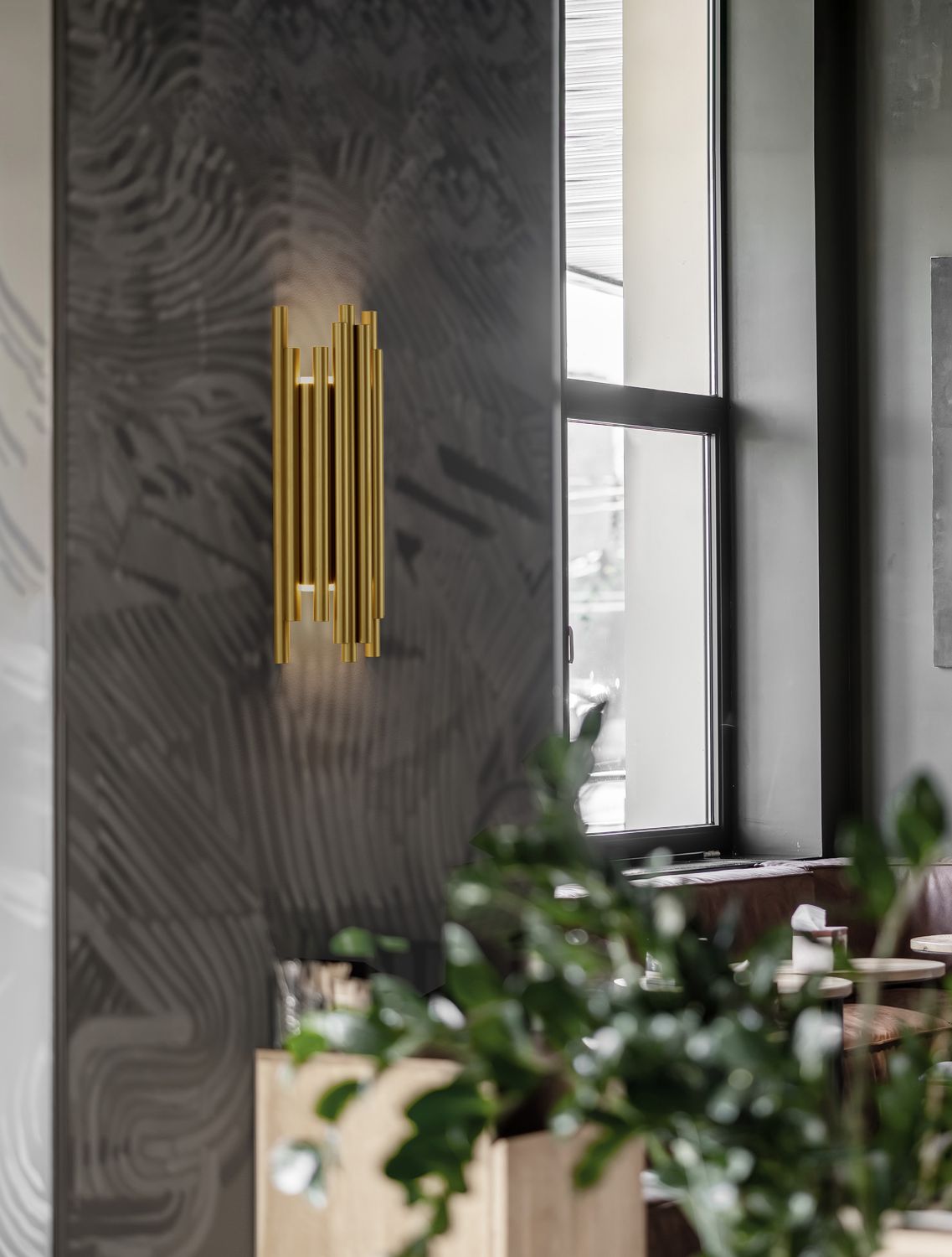 Mise en ambiance d'une applique dorée sur un mur texturé près d'une fenêtre