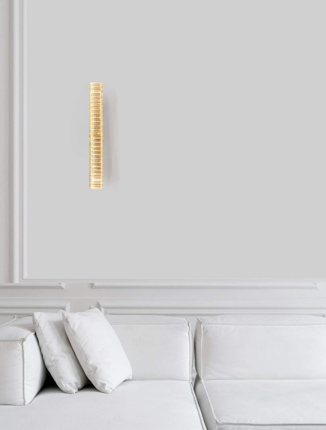 Applique murale dorée et cristal allumée, fixée sur un mur blanc au-dessus d'un canapé.
