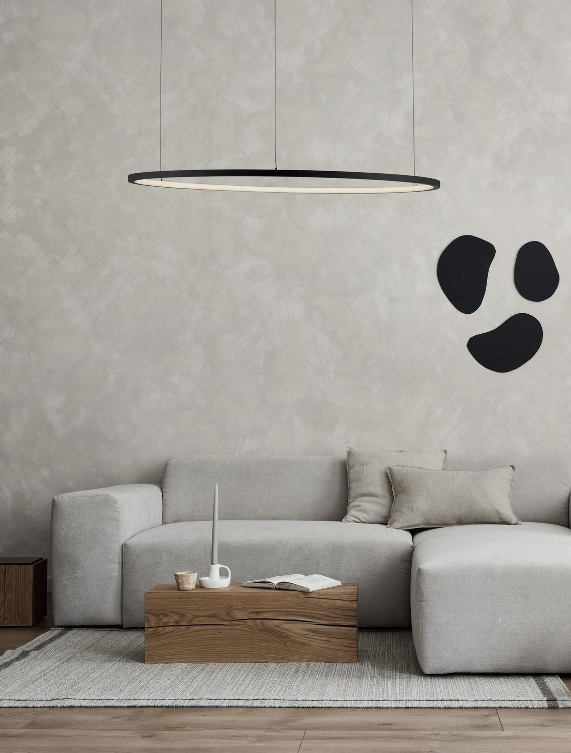 Suspension anneau noir allumée au-dessus d'un canapé gris, salon au mur béton