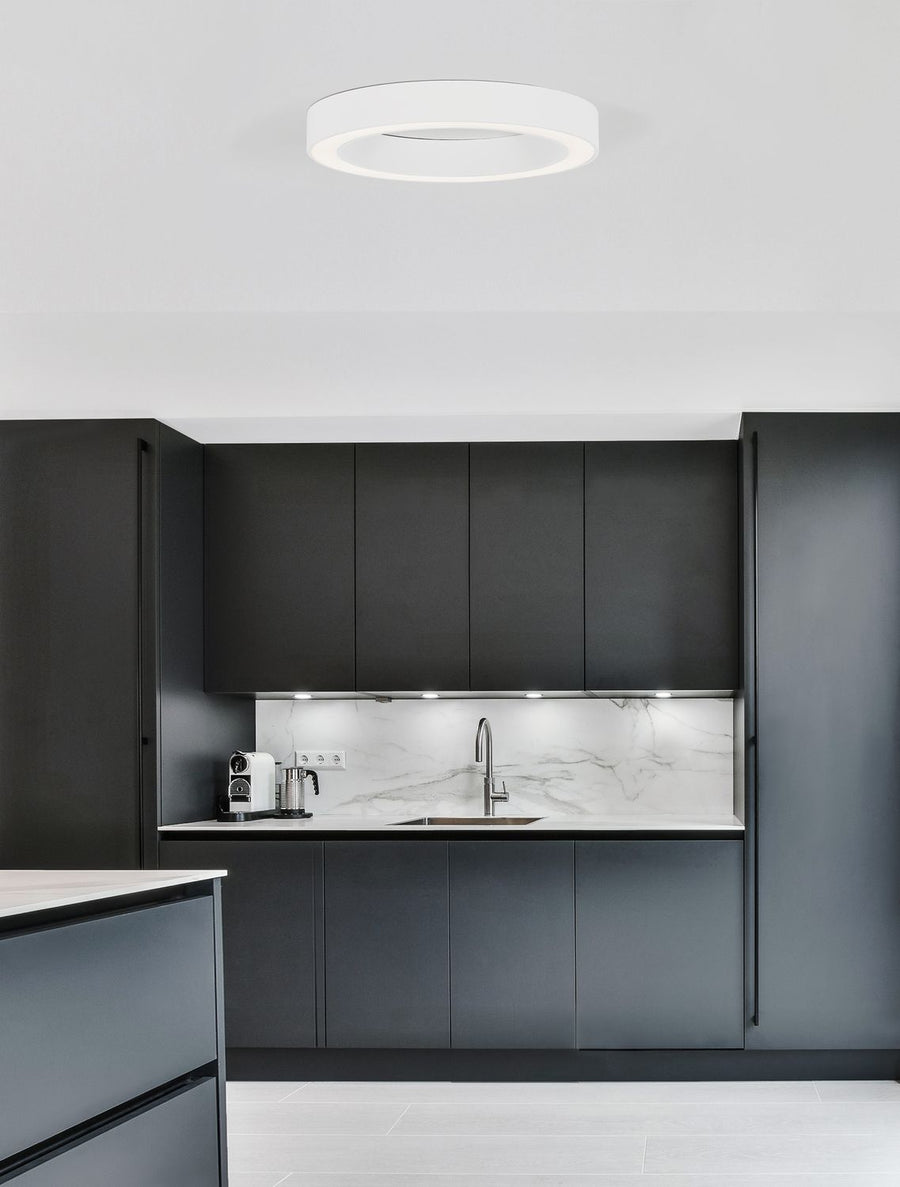 Plafonnier blanc circulaire installé au plafond d'une cuisine moderne aux meubles noirs